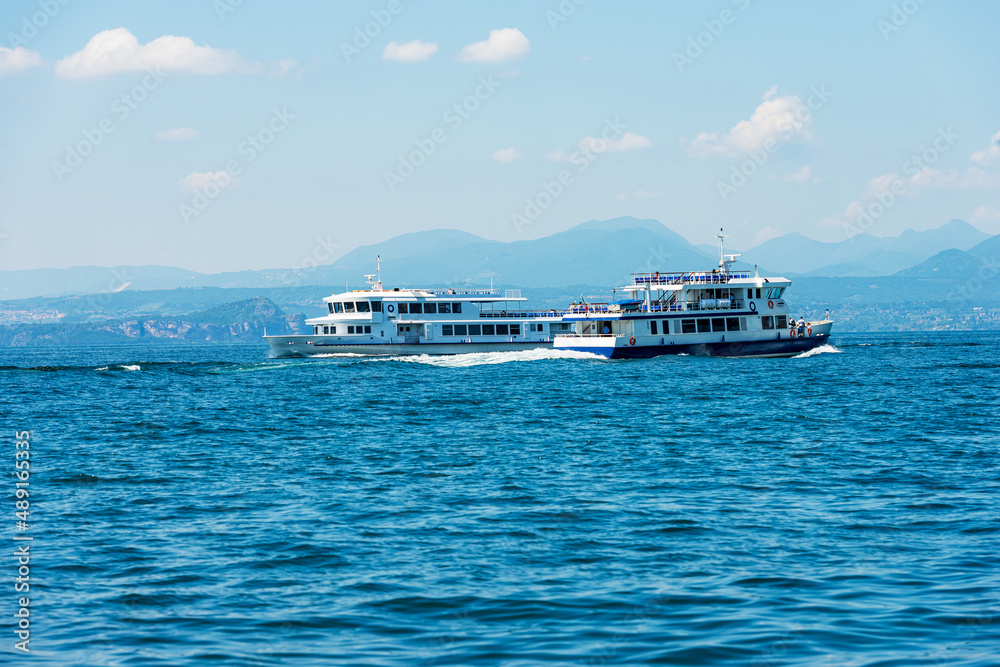 Two ferry boats in motion on Lake Garda (Lago di Garda), in front of the small village of Bardolino, Verona province, Veneto, Italy, Europe. On the horizon the coast of Lombardy with the mountains.