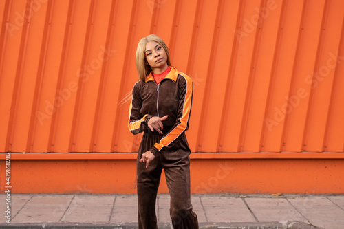 Una alegre mujer afroamericana con ropa deportiva bailando en la calle sobre un fondo naranja photo