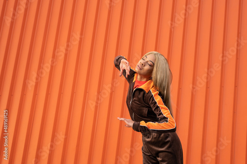 Una alegre mujer afroamericana con ropa deportiva bailando en la calle sobre un fondo naranja photo