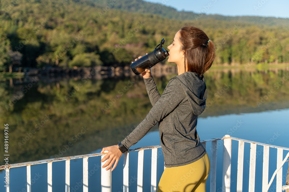 Obraz premium Young attractive and active woman drinking water from her plastic water bottle while taking a break from her healthy early morning running exercise