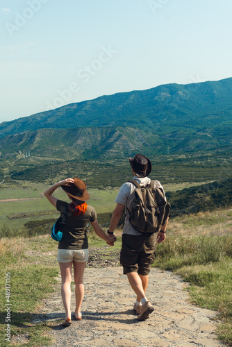A couple of tourists in hats, a man with a backpack. walk against the backdrop of the mountains. Mtskheta. Georgia. Vertical photo