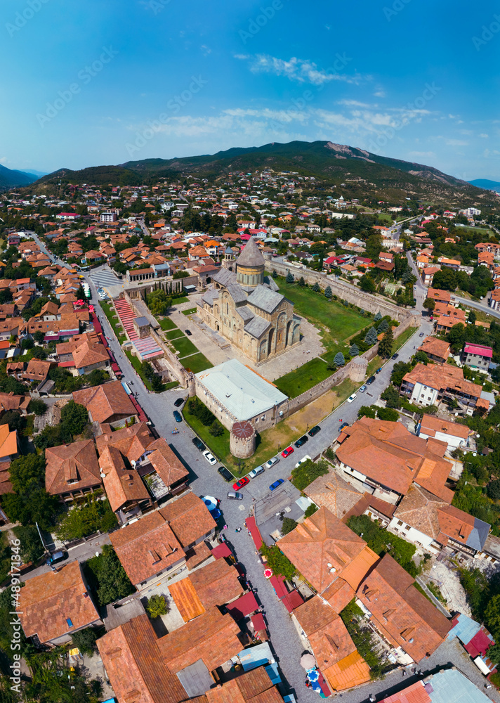 Beautiful aerial view of streets of Mtskheta village in Georgia. Mtkvari river. Summer sunny day. Travel and vacation. Svetitskhoveli Cathedral fortress in the center. Vertical photo