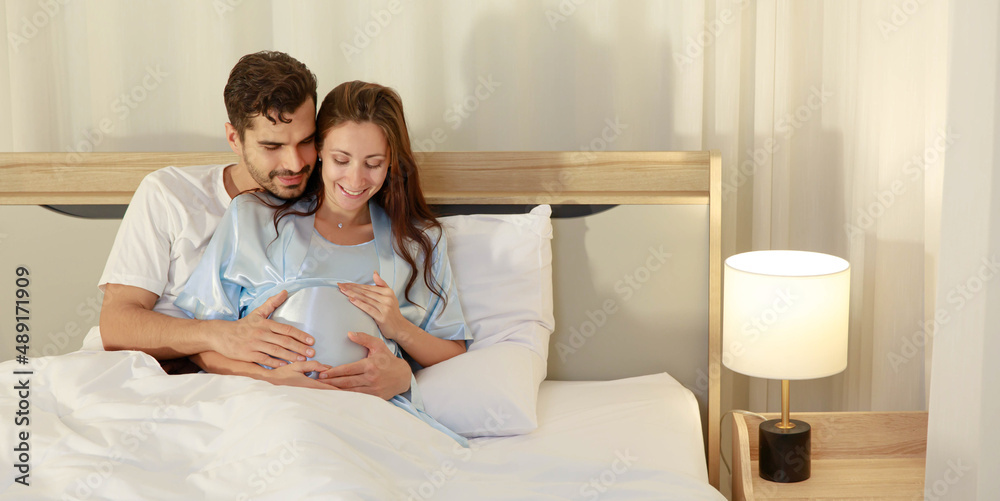 Cheerful husband enjoy embracing pregnant wife and happy to tenderly fondle beloved belly of unborn baby and expecting warm family during prenatal care of maternity at romantic bedroom Cheerful husband enjoy embracing pregnant wife and happy to tenderly fondle beloved belly of unborn baby and expecting warm family during prenatal care of maternity at romantic bedroom