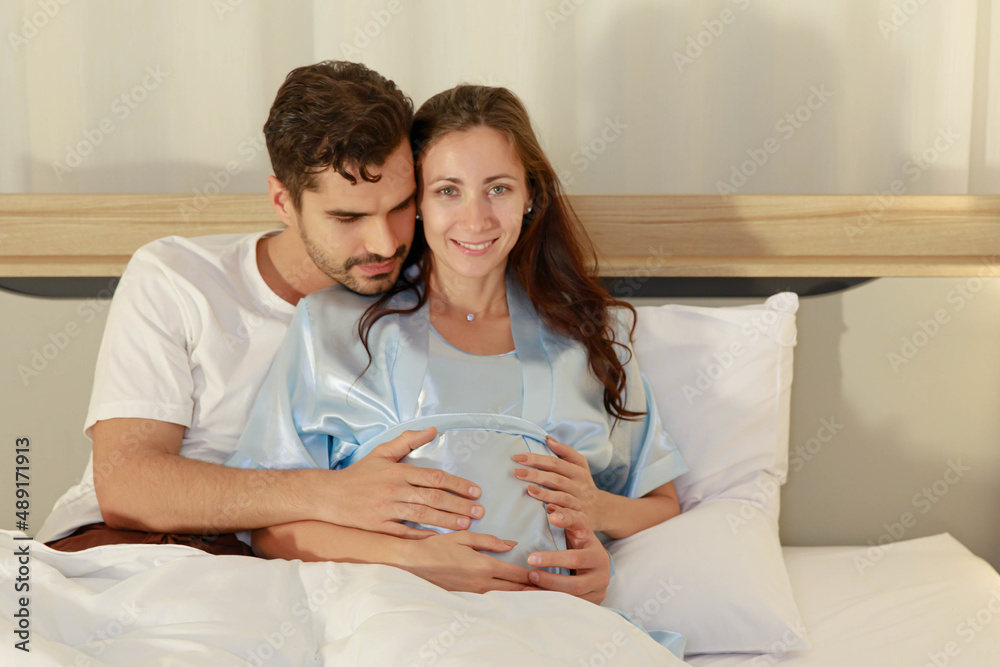 Cheerful husband enjoy embracing pregnant wife and happy to tenderly fondle beloved belly of unborn baby and expecting warm family during prenatal care of maternity at romantic bedroom Cheerful husband enjoy embracing pregnant wife and happy to tenderly fondle beloved belly of unborn baby and expecting warm family during prenatal care of maternity at romantic bedroom