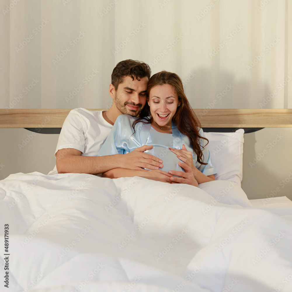 Cheerful husband enjoy embracing pregnant wife and happy to tenderly fondle beloved belly of unborn baby and expecting warm family during prenatal care of maternity at romantic bedroom Cheerful husband enjoy embracing pregnant wife and happy to tenderly fondle beloved belly of unborn baby and expecting warm family during prenatal care of maternity at romantic bedroom