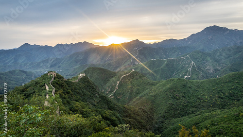Bergpanorama an der chinesischen Mauer: die ersten Lichtstrahlen der aufgehenden Morgensonne brechen durch die Wolken und färben die chinesische Mauer am Mauerabschnitt Jiankou in ein zartes rot
