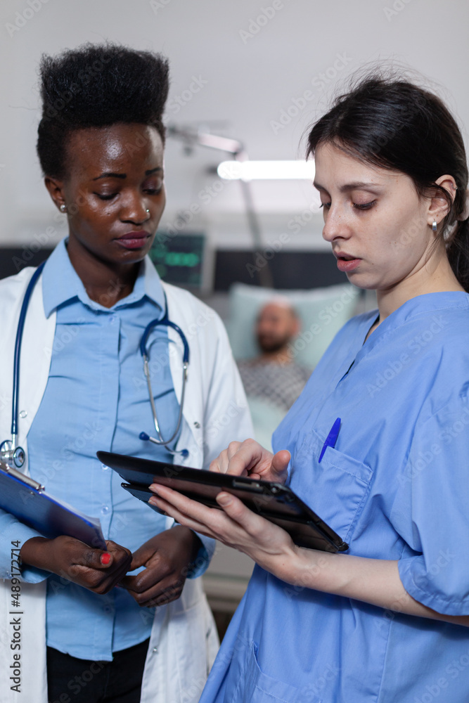 Fototapeta premium Nurse showing lab results from digital tablet to doctor holding clipboard with medical history in modern hospital ward. Health care specialists using modern technology for clinical diagnosis.