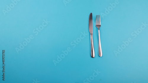 Crossed steel knife and fork on tredny soft blue paper background with side copy space