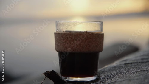 Coffee in a sustainable keep cup out of glass placed on a tree at sunrise in the morning. Lake in the Background. 4K Sunrise. Sustainable.  photo