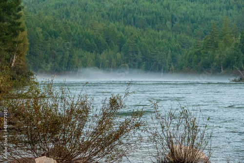 fog over the water of a mountain river on the background of a forest and a mountain