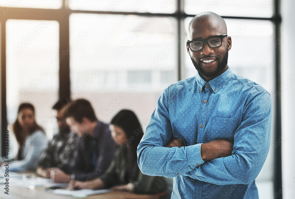 Obraz premium Were always ready to help you succeed. Portrait of a cheerful businessman posing with his arms folded in a modern office with his colleagues in the background.