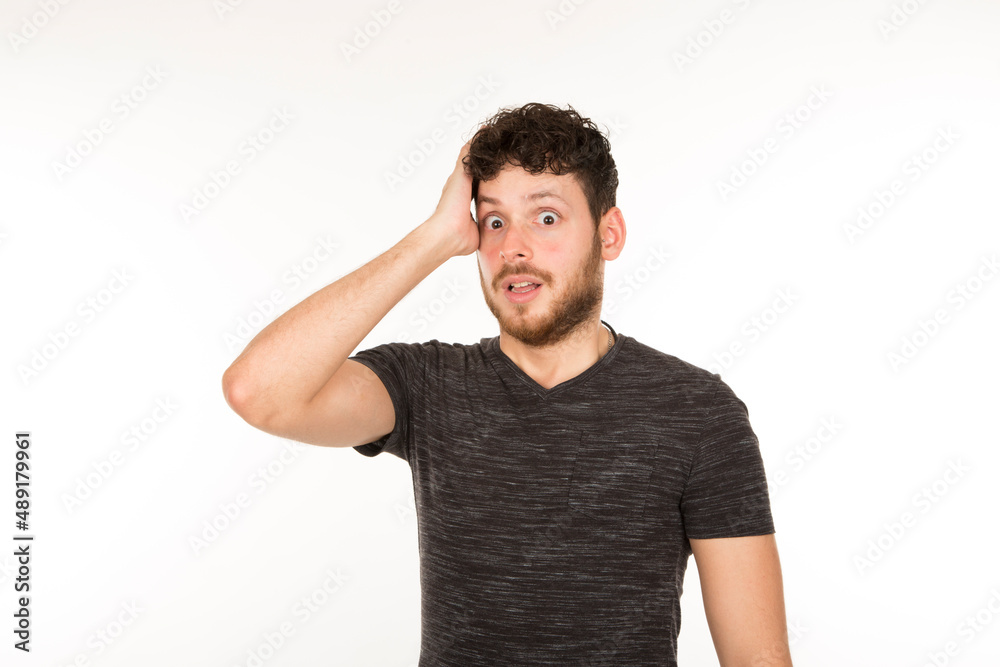 young bearded man with hand on head with expression of surprise and astonishment on white background young bearded man with hand on head with expression of surprise and astonishment on white background