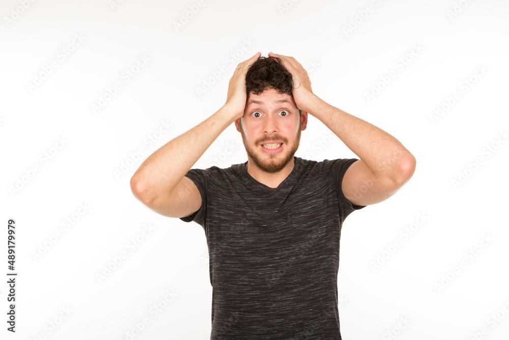 young bearded man with hands on head with surprised and frightened expression on white background young bearded man with hands on head with surprised and frightened expression on white background