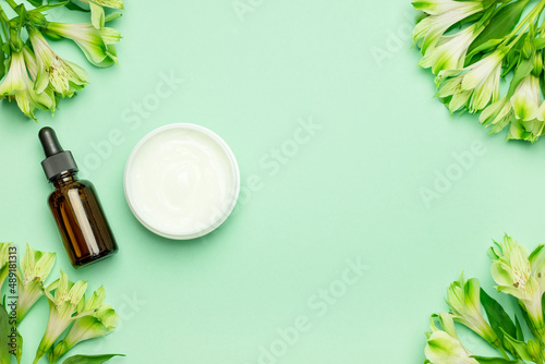 Skin care products, natural cosmetic. Flat lay image on green background Natural cosmetic skincare bottle, serum and flowers. Homemade and beauty product concept.