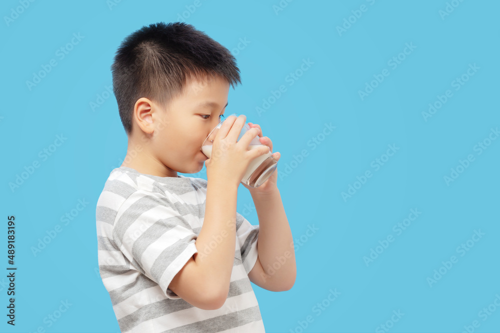 Kid drinking milk in glass on blue background Kid drinking milk in glass on blue background