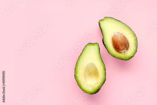 Flat lay of one halved fresh avocado over minimal pink background. Raw natural food.