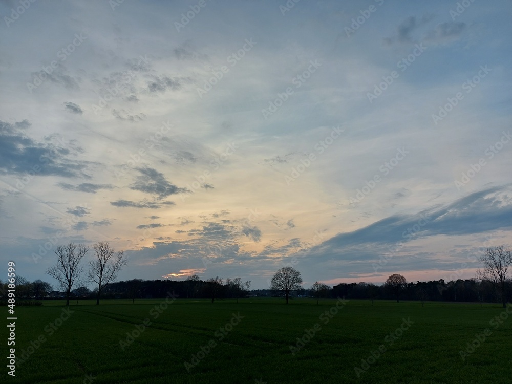 Sonnenuntergang, gefolgt von bunten Wolken. Der Himmel über den schlafenden Feldern und Bäumen. Die Natur malt den Himmel und löscht ihn aus. Romantische Szenen für Hintergründe. Dämmerung in Rottönen