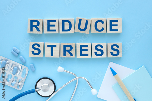 REDUCE STRESS text on wooden cubes on a blue background. pen blue tablet stethoscope Flat lay. Marketing concept.
