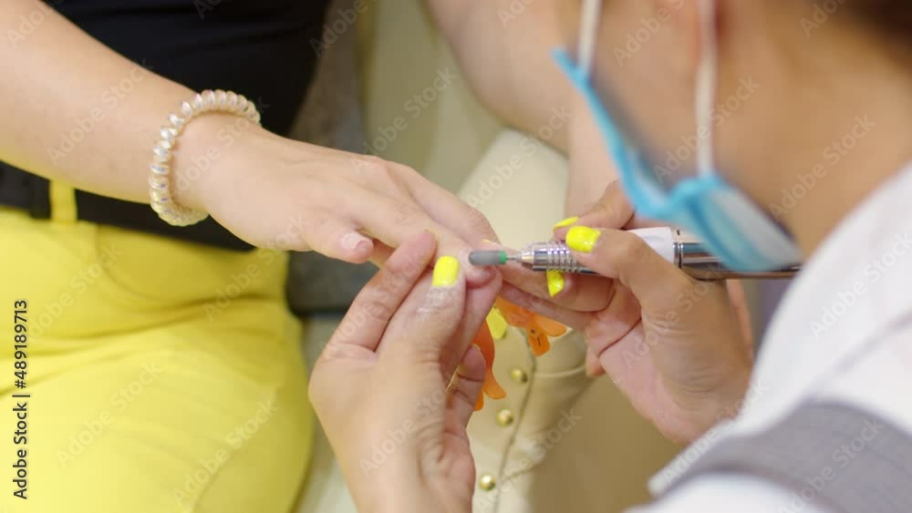 Beautician makes a manicure to a brunette in a hairdressing salon. Woman beautician makes the procedure, prepares and processes the client's nail with a special scalpel to remove old nail polish. Beautician makes a manicure to a brunette in a hairdressing salon. Woman beautician makes the procedure, prepares and processes the client's nail with a special scalpel to remove old nail polish.
