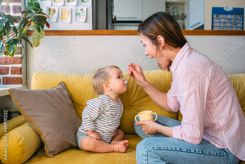 Mom feeds a small child at home with yogurt from a spoon. Family concept