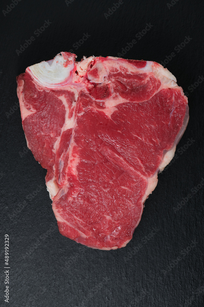 Raw fiorentina steak on black slate flat lay. Fiorentina steak on black background copy space. A piece of raw beef meat on a black stone table, flat lay. Raw fiorentina steak on black slate flat lay. Fiorentina steak on black background copy space. A piece of raw beef meat on a black stone table, flat lay.