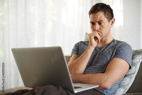 Now thats a thinker. Shot of a handsome young man using his laptop at home.