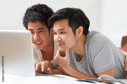 Finding everything theyre looking for.... Two young Asian guys searching the internet together on a laptop.