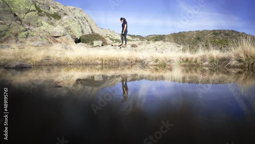 asiatic young trekker woman explore scenic natural landscape in penalara natural park Madrid Spain, rocky mountains peak reflection on flat water surface of high altitude lake photo