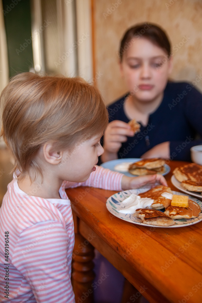 Toddler girl with older sister at breakfast table eating pancakes. Toddler girl with older sister at breakfast table eating pancakes.