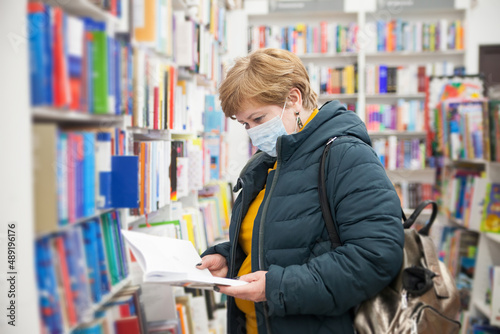  Mature woman in medical mask among bookshelves in store