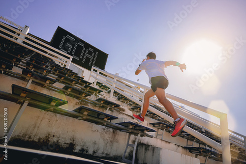 Young man running sprinting up stairs at stadium with GOAL text in scoreboard. Fit runner fitness runner during outdoor workout. Selected focus