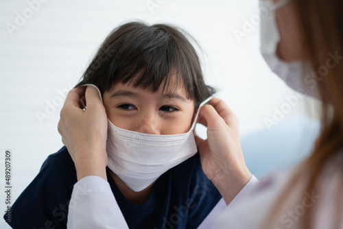 Asian parents wear face masks to little daughter for protection against coronavirus covid 19 before going to school. Mom teaches daughter to put on a medical mask