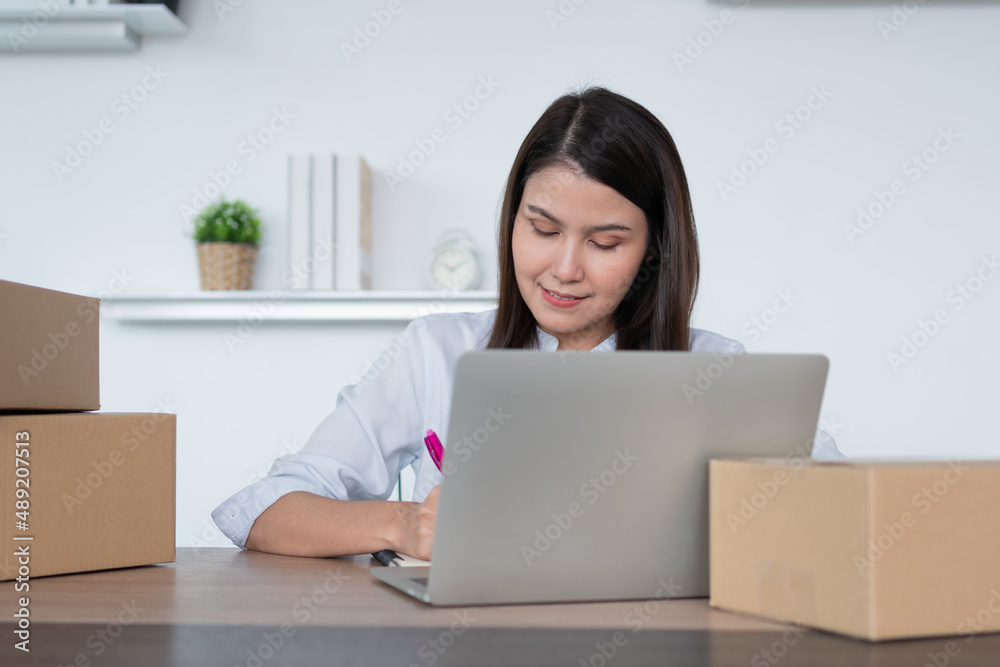 Happy young Asian woman entrepreneur, Take note after check order and Smile for sale success of online shopping store, Concept of the merchant, small business, online business, and eCommerce. Happy young Asian woman entrepreneur, Take note after check order and Smile for sale success of online shopping store, Concept of the merchant, small business, online business, and eCommerce.