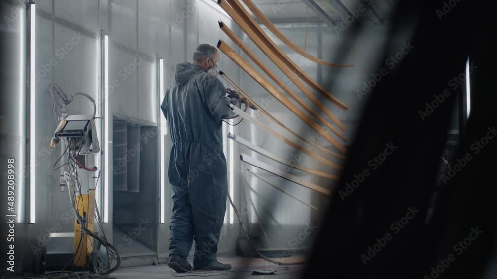 Slow motion: A man in a protective suit and mask painter sprays paint on the parts. Small business painting shop. Workshop for painting parts. Slow motion: A man in a protective suit and mask painter sprays paint on the parts. Small business painting shop. Workshop for painting parts.