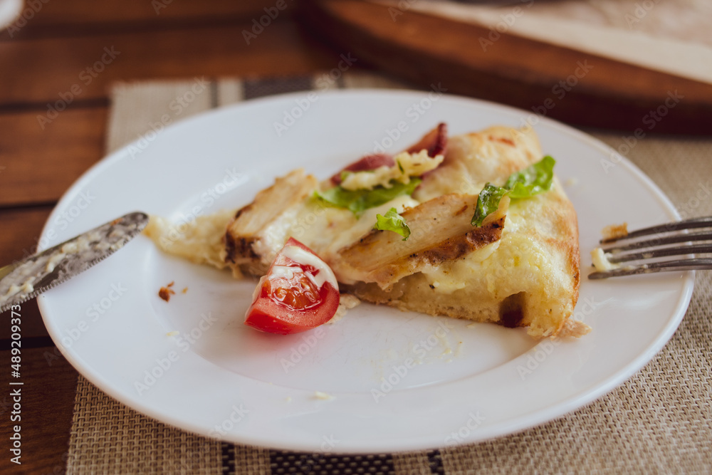 A piece of pizza with tomatoes, cheese and bacon on a white plate close-up.