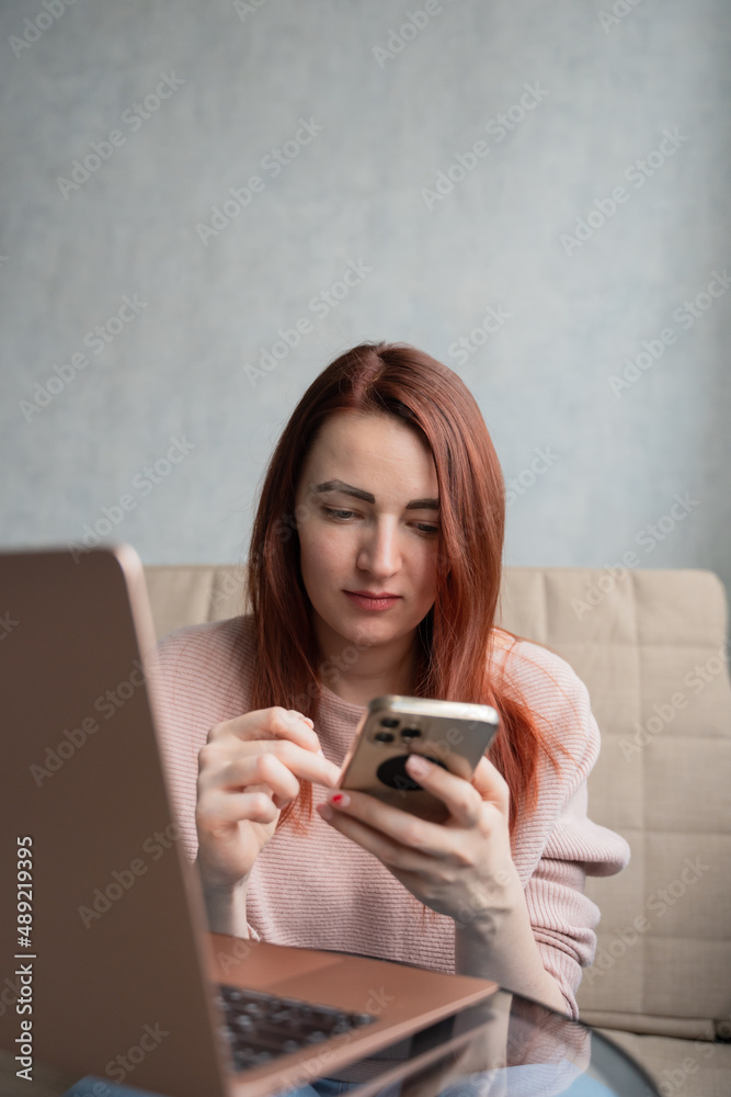 Redhead young woman sitting on sofa with laptop and smartphone. Redhead young woman sitting on sofa with laptop and smartphone.