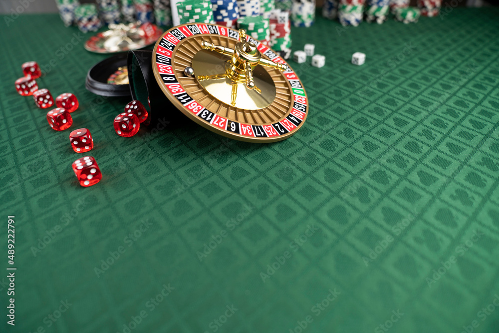 Casino. Gambling games theme. Roulette wheel, dice and poker chips on the casino felt green table. Casino. Gambling games theme. Roulette wheel, dice and poker chips on the casino felt green table.