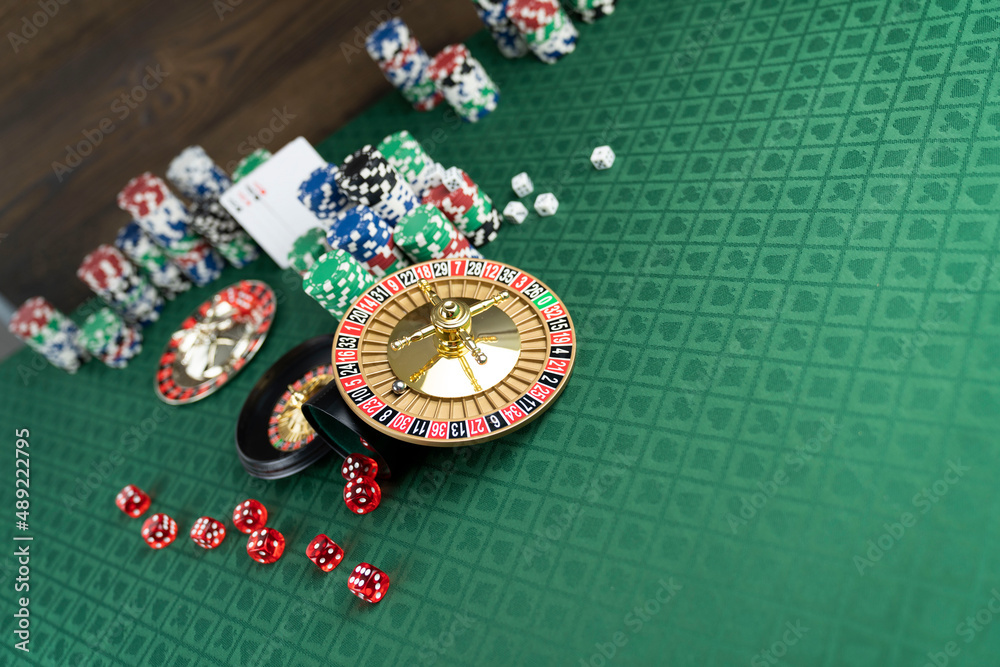 Casino. Gambling games theme. Roulette wheel, dice and poker chips on the casino felt green table. Casino. Gambling games theme. Roulette wheel, dice and poker chips on the casino felt green table.