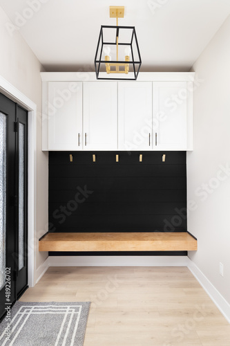 A modern farmhouse entryway with bench seating, black shiplap, white cabinets, gold coat hooks, and a black and gold light fixture.
