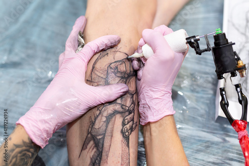 Close-up of the tattoo machine. A tattoo. A male master in a mask and gloves creates a pattern on the skin of a woman.