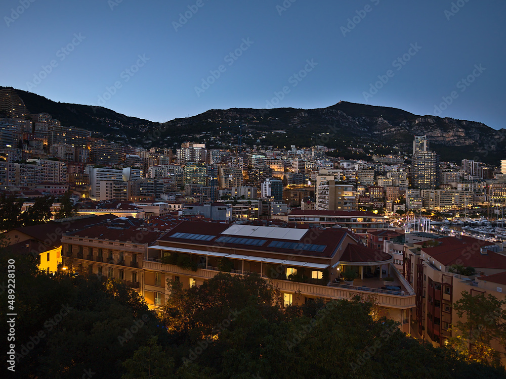 Beautiful panoramic view over the downtown of Monaco at the French Riviera in the evening with illuminated residential apartments buildings and hills.