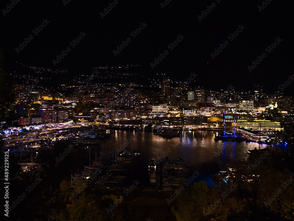Fototapeta premium Stunning night view of the downtown of Monaco at the mediterranean coast with funfair and yacht boats moored in marina Port Hercule with buildings.