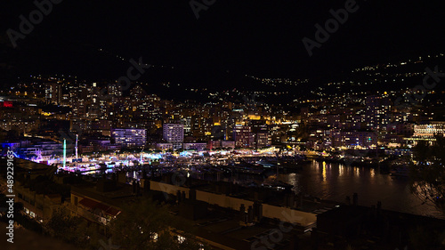 Beautiful night view of the harbor of Monaco (Port Hercule) at the French Riviera with colorful funfair surrounded by illuminated apartment buildings.