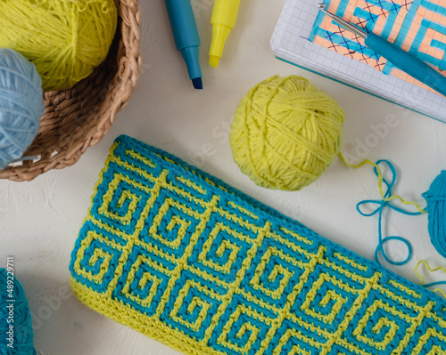 Yellow blue crochet fabric with mosaic pattern. Workplace with crochet fabric, yarn balls, crochet hook, notebook and markers. photo
