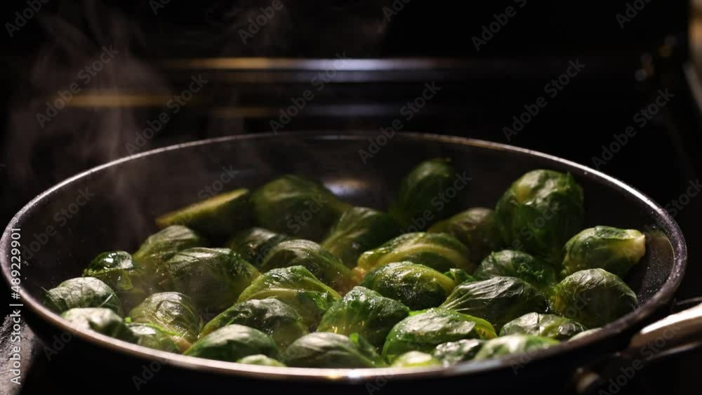 Steam coming from hot brussels sprouts while cooking in a pan. Vegan cooking, close up, dark mood shot. Steam coming from hot brussels sprouts while cooking in a pan. Vegan cooking, close up, dark mood shot.