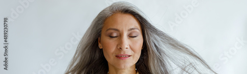 Canvas Print Pretty tranquil Asian woman with flying silver hair stands on light grey background in studio
