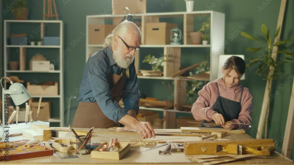 Grandfather Carpenter with Granddaughter Work with Wood to Create Items or Furniture Using Carpentry Tools. Training in Craft Skills in Home Workshop. Communication of Generations. Handicraft, Hobby. Grandfather Carpenter with Granddaughter Work with Wood to Create Items or Furniture Using Carpentry Tools. Training in Craft Skills in Home Workshop. Communication of Generations. Handicraft, Hobby.