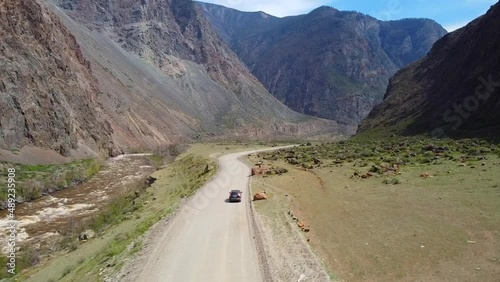 The car is driving off-road among the mountains. Video from a mountain valley drone.