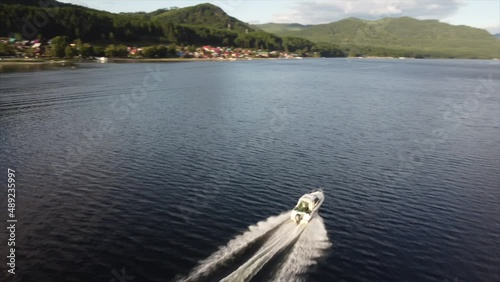 the boat goes through the water at high speed among the mountains of houses and forests. Drone video.