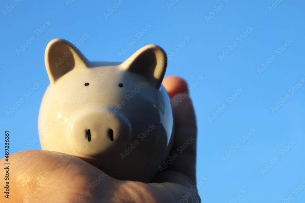 Man holding piggy bank carefully on blue backgound, saving money for retirement concept.